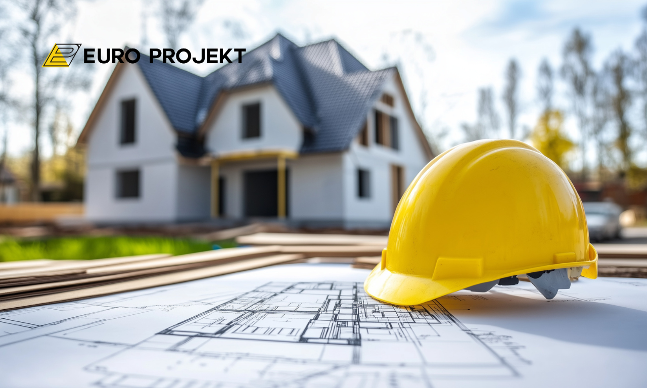 Żółty kask budowlany leżący na rysunkach projektowych, w tle dom jednorodzinny w budowie