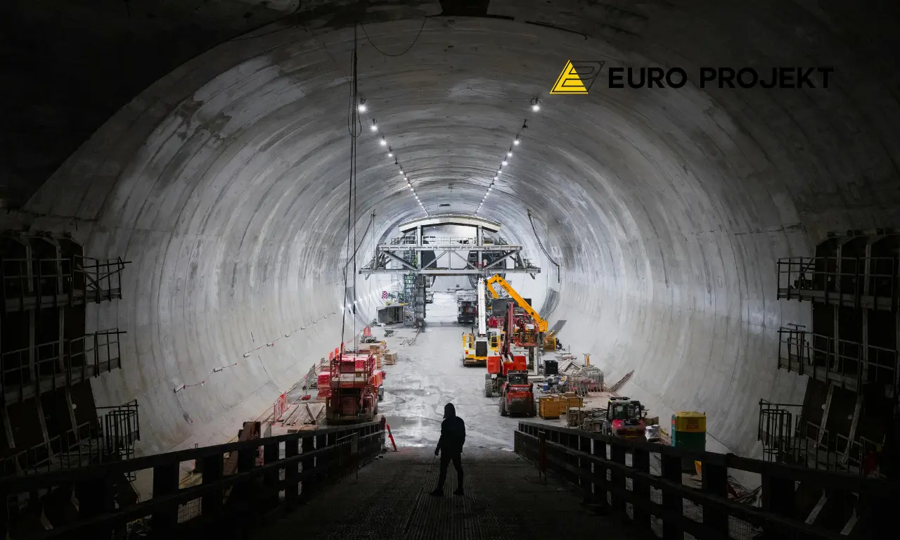 Wnętrze tunelu drogowego w budowie z żelbetową obudową, maszynami i oświetleniem